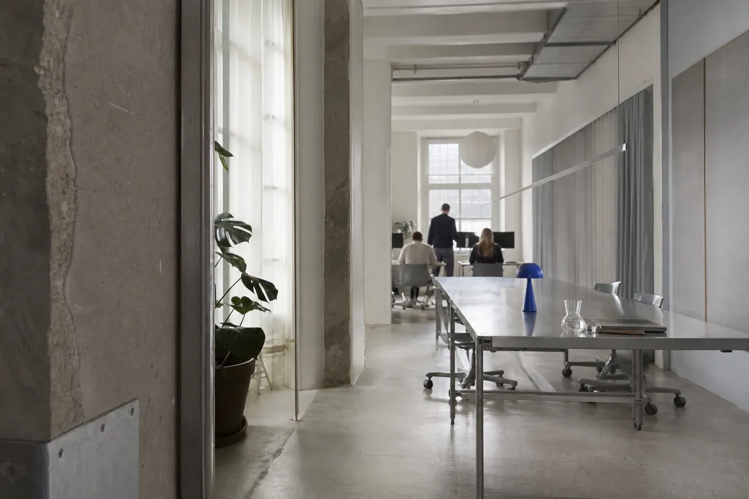 Editorial studio environment with a distant, out-of-focus team and a long shared table